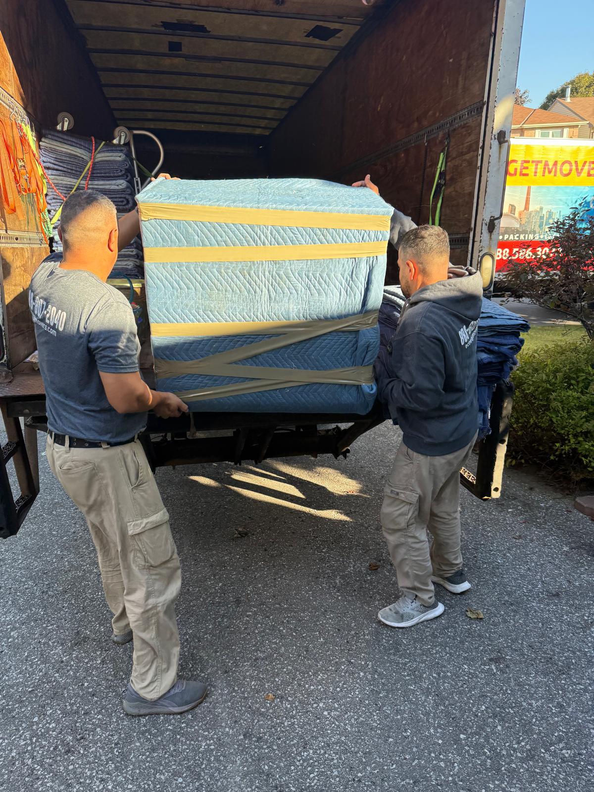 Ecoway Movers Burlington two-person crew carrying a sofa through a Burlington home doorway with floor protection visible